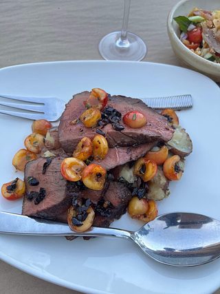 Sliced beef tenderloin topped with cherries and prune on a bed of young potatoes.