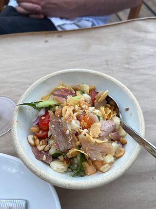 A bowl of smoked fish with assorted nuts, tomatoes, and mixed greens.