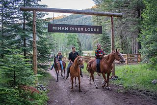 Horseback riders beneath a gate with a sign reading “Minam River Lodge”